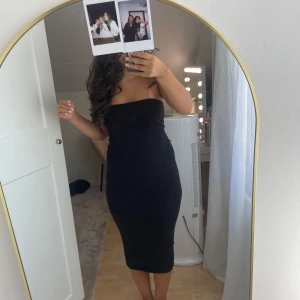 Svart axelbandslös långklänning - Säljer en stilren svart axelbandslös långklänning med figurnära passform. Klänningen har en enkel och elegant design som sitter snyggt över kroppen och slutar vid vaden. Perfekt för dig som gillar minimalistisk stil och vill ha en klassisk look.