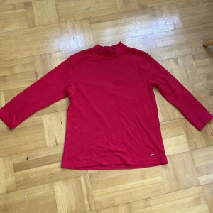 Röd polotröja från Flash Essential - Säljer en röd polotröja från Flash Essential i ekologisk bomull. Tröjan har lång ärm och en enkel, clean design utan mönster eller detaljer. Perfekt för dig som gillar basic och vill ha en skön tröja med lite högre hals. Storlek L.