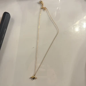Guldigt halsband med hjärtberlock - Snyggt och tunt halsband i guld med en liten hjärtformad berlock som har en unik detalj på sidan. Perfekt för dig som gillar minimalistiska smycken med en twist. Kedjan är enkel och stilren, och berlocken ger en personlig touch.