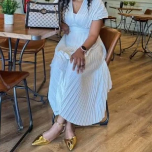 Vit långklänning med omlott och plissering - Säljer en elegant vit långklänning med omlott-design och v-ringad hals. Klänningen har korta ärmar och är plisserad för en snygg flowy look. Perfekt för dig som gillar stilrena och romantiska vibes. Passar dig som vill sticka ut med en klassisk och fräsch outfit.