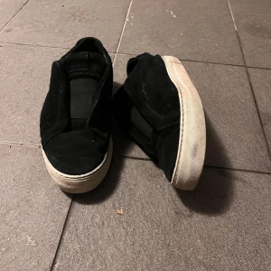 Svarta sneakers från Axel Arigato - Svarta slip-on sneakers från Axel Arigato i mocka med vit platt sula. Skorna har en minimalistisk design med bred resår över vristen och rund tå. Perfekta för en clean och stilren look.