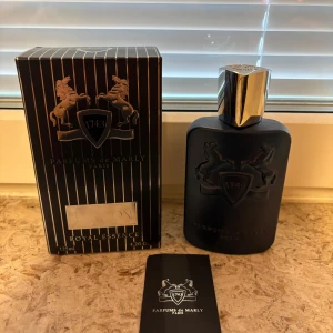 Parfums de Marly Layton 125ml - Lyxig parfymflaska från Parfums de Marly, Layton Royal Essence, 125ml. Flaskan är matt mörkblå med silverfärgat lock i metall och har en elegant, rektangulär form med ingraverade hästar och sköld. Kommer med originalförpackning i svart med silverdetaljer.