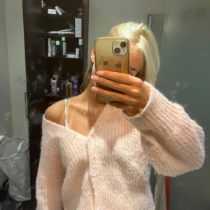 Ljusrosa stickad kofta med knappar - Supermysig ljusrosa stickad kofta med tre knappar framtill och lite oversized passform. Koftan har långärmade ärmar och en djup v-ringning som gör att den sitter snyggt offshoulder. Perfekt att slänga på sig när man vill vara både chill och söt.