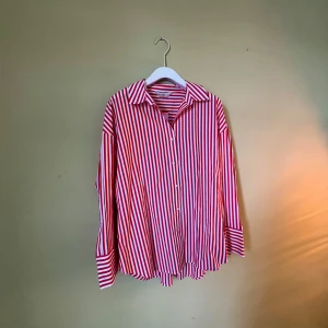 Rödvit randig skjorta från F&F - Snygg skjorta från F&F med rödvita vertikala ränder och klassisk krage. Modellen är loose fit med långa ärmar och knappar framtill. Tillverkad i mjuk bomull som känns skön mot huden. Perfekt för dig som gillar färg och mönster.