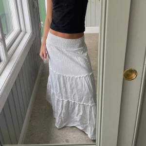 Vit långkjol med volanger - Supersöt vit långkjol med smock i midjan och flera volanglager. den är från vero moda