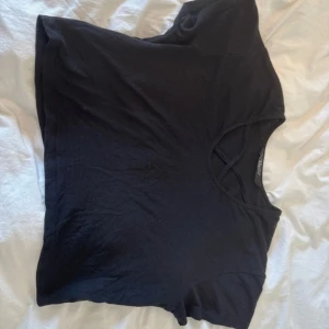 Svart croppad topp från New Look - Svart croppad topp från New Look med snygga korsade band vid halsringningen. T-shirten har korta ärmar och är gjord i mjuk bomull, perfekt för en chill och stilren look. Passar dig som gillar enkla men coola detaljer.