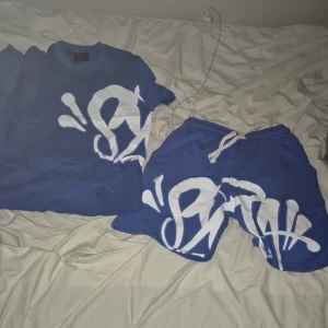 Syna world set - Blå t-shirt och blåa shorts med stor vit graffiti print från syna world Tshirten har rund hals och korta ärmar, tillverkad i mjuk bomull. Perfekt för dig som gillar streetwear och vill sticka ut med en fet design.