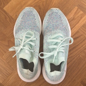 Mintgröna/färgglada sneakers - Säljer ett par mintgröna sneakers med stickad ovandel och snörning. Skorna har en vit platt sula och ett randigt mönster i blått, rosa och lila på ovansidan. Superlätta och luftiga, perfekta för dig som gillar sportig stil och vill ha något som sticker ut.