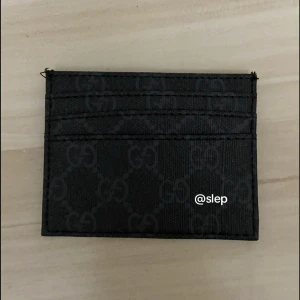 Svart plånbok med GG-mönster - Snygg svart plånbok med klassiskt GG-mönster över hela ytan. Slimmad design med flera kortfack, perfekt för dig som vill ha stil och funktion i fickan. Materialet är slitstark syntet och plånboken har en modern look som passar till allt.