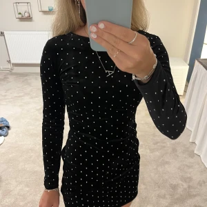 Svart prickig sammetsklänning H&M XS - Supersnygg svart kort klänning från H&M i mjuk sammet med vita prickar över hela. Den har en liten öppnad rygg och är i väldigt fint skick. Använd en gång, perfekt på nyår! 