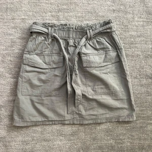 Snygg kamouflagegrön kargokjol  - Säljer nu denna coola kamouflagegröna tygkjol med resår i midjan och ett band runt som går att knyta. Kjolen köptes för 250 kr men säljer nu för 49 kr!💗