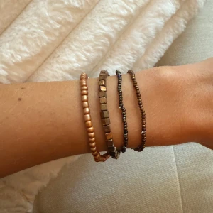Bruna och bronsfärgade pärlarmband - Fyra stretchiga armband med små pärlor i bruna och bronsiga toner. Två armband har runda pärlor och två har små fyrkantiga pärlor, vilket ger en cool mixad look. Perfekt att bära tillsammans eller var för sig för en avslappnad stil. Dom är separata men säljs tillsammans.
