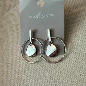 Silvriga örhängen  - Ett par silverfärgade örhängen med hängande detaljer. Obs det är inte samma märke som det står på lappen.