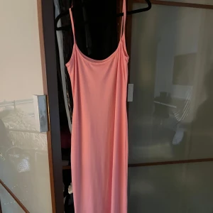 Lång rosa klänning med smala axelband - Säljer en enkel och stilren lång klänning i mjuk rosa färg. Klänningen har smala axelband och rak passform som faller snyggt längs kroppen. Aldrig använt!
