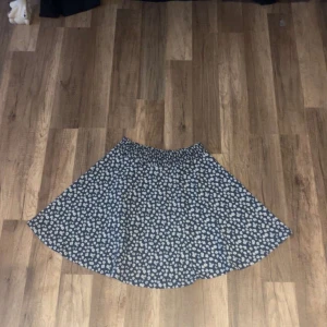 Blommig blå kjol från 157 XS - Supersöt blå kjol med vita blommor från 157 i storlek XS. Kjolen har en kort längd och ett elastiskt midjeband som gör den bekväm och enkel att bära. Perfekt för dig som gillar blommigt och vill ha en flowy look.