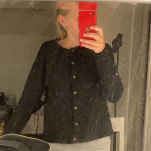 Svart kofta med knappar - Svart kofta med rund hals och snygga knappar hela vägen framtill. Långärmad och lätt ribbad i materialet, perfekt att slänga över en topp. Enkel och stilren design som funkar till många olika looks.