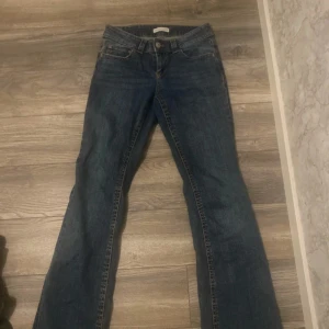Blå bootcut jeans från Gina Tricot - Snygga blå jeans från Gina Tricot, modell Perfect Jeans i storlek 36. Klassisk femficksdesign med silverfärgade knappar och bootcut-ben som ger en schysst siluett. Jeansen har låg midja och är gjorda i slitstarkt denim med kontrastsömmar.