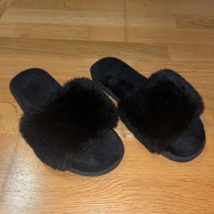Svarta fluffiga sandaler  - Svarta sandaler med bred rem täckt av mjukt, fluffigt pälsmaterial., storlek 38-39.