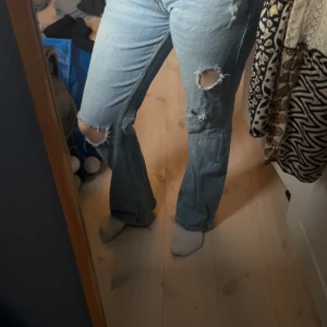 Bootcut ljusblå jeans med slitningar - Säljer ett par ljusblå bootcut jeans med snygga slitningar och hål vid knäna. Jeansen har klassisk femficksdesign och är tillverkade i jeansmaterial. bootcut jeans stl 36