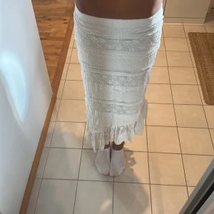 Vit långkjol med spets och volang - Superfin vit långkjol med spetsdetaljer och volang längst ner. Kjolen har ett romantiskt och bohemiskt uttryck med flera lager av spets och broderade blommor. Perfekt för sommarens alla tillfällen och ger en riktigt fräsch vibe. Kjolen är använd vid ett tillfälle och är väldigt fin till sommaren.