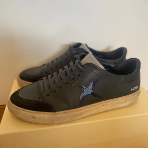 Mörkblå sneakers från Axel Arigato - Snygga mörkblå sneakers från Axel Arigato med broderad fågel, nypris 2300 kr. Den har flera små defekter men inget man ser på håll. Kommer med skolåda, påse och rengörings servetter. Påsen har klistermärken på baksidan.