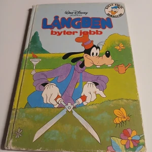 Disneybok – Långben byter jobb (1980) - Följ med Långben på hans tokiga äventyr när han testar nya jobb tillsammans med vänner som Musse Pigg och Kalle Anka. En färgglad och rolig berättelse fylld av humor och klassiska Disney-karaktärer – perfekt för dig som gillar skojiga historier och tecknade figurer! Lite slitage på omslaget men fin invändigt 