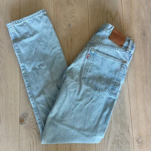Levi's 504 ljusblå jeans W26 L30 - Säljer ett par Levi's 504 jeans i ljusblå tvätt med klassisk femficksdesign och knappgylf. Jeansen har raka ben och normal passform, med brunt läderpatch bak i midjan och den ikoniska röda Levi's-taggen på bakfickan. Perfekt för dig som gillar retrovibe och tidlös stil.