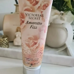 Victoria's Secret Amaretto Fizz lotion - Fragrance lotion från Victoria's Secret i doften Amaretto Fizz. Tuben rymmer 236 ml och har en snygg design med rosa och guldiga detaljer. Doftnoter av mandelkaffe och apelsinblomma. Perfekt för dig som gillar lyxiga och söta dofter. Helt ny och oanvänd