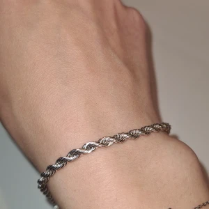 Pilgrim flätat silverfärgat armband - Snyggt pilgrim armband i silverfärg med flätad design. Kedjan är tvinnad och ger ett stilrent och modernt intryck. Perfekt accessoar för att lyfta din outfit med en enkel men elegant detalj. Små tycken på missfärgning.