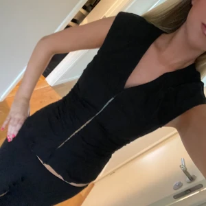 Svart korsett-topp weekday  - Snygg svart korsett-topp med v-ringad hals och korta ärmar. Toppen har en figurnära passform och knappar framtill som ger en cool detalj. Perfekt att styla med jeans eller kjol för en trendig look. Inprincip oanvänd