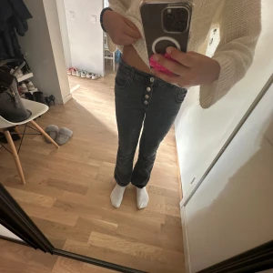 Svarta bootcut jeans från Zara - Snygga svarta jeans från Zara som jag har växt ut men har bootcut passform och hög midja. Jeansen har fyra silverfärgade knappar framtill, klassiska fickor och är gjorda i mjukt denimtyg. Perfekta för dig som gillar en stilren look med lite edge.
