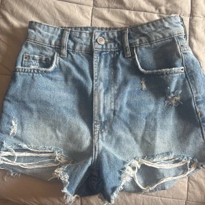 Blå jeansshorts från Zara - Snygga blå jeansshorts från Zara, slitna kanter med medelhög midja. Storlek 32 i bra skick. 