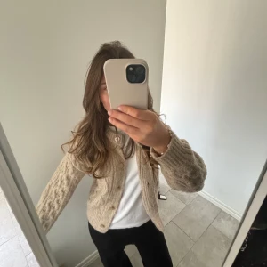 Beige stickad kofta från Zara - Säljer en beige stickad kofta från Zara med ett klassiskt flätmönster. Koftan har långa ärmar och knappar framtill. Passar s/m