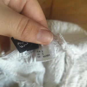 Vit offshoulder topp - Säljer en söt vit offshoulder topp med smockdetaljer. Toppen är croppad och har en elastisk passform som gör den bekväm att bära. Perfekt för varma sommardagar!