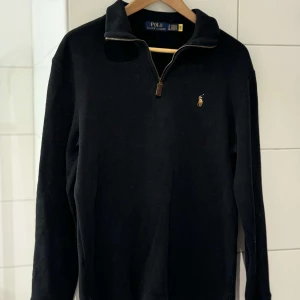 Svart half zip från Polo Ralph Lauren - Säljer en stilren svart tröja från Polo Ralph Lauren med dragkedja och det klassiska logotypbroderiet på bröstet. Tröjan har långa ärmar och en hög krage som ger en sportig look. Perfekt för en avslappnad stil. Nypris ca 2300 och jag har bara använt den ett fåtal gånger.