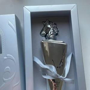 Lattafa Maahir leagcy 100ml - Elegant parfymflaska i silver med ett detaljerat hästhuvud som lock. Flaskan har en unik och lyxig design, perfekt för den som vill ha något utöver det vanliga. Kommer i en stilren förpackning med fönster som visar flaskans design. 70-80% kvar!