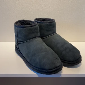 Svarta boots från UGG - Säljer ett par svarta UGG boots i mocka med mjukt foder. Perfekta för kalla dagar med sin varma och bekväma design. De har en robust sula för bra grepp och en klassisk UGG-logga på baksidan.