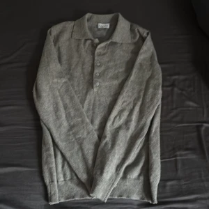 Grå långärmad pikétröja - Säljer en stilren grå långärmad pikétröja med knappar framtill. Perfekt för en avslappnad men ändå snygg look. Tröjan har en klassisk krage och ribbade muddar vid ärmslut och nederkant. 100% cashmere