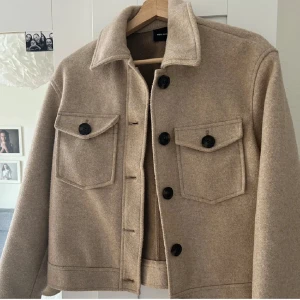 Kappa  från Vero Moda - Snygg beige jacka från Vero Moda med stora svarta knappar och två bröstfickor. Jackan har en klassisk krage och är perfekt för höst och vår. Den är tillverkad i ett mjukt material som ger en stilren look. M men passar som S, pris kan diskuteras‼️