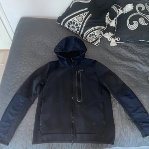 Nike Tech Fleece Hoodie - Säljer en sällsynt svart/reflektiv Nike tech fleece hoodie med bröstficka, Väldigt bra skick och storleken är Medium. Kontakta mig vid fler frågor