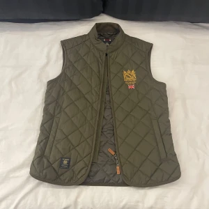 Morris väst - Mörkgrön Morris Quilted väst. | Västen är i super bra skick. | Den har en inner ficka i manchester samt två fickor med knappar på utsidan. | Det är bara att höra av sig om man har några frågor eller om man vill ha flera bilder🍸🍸🍸
