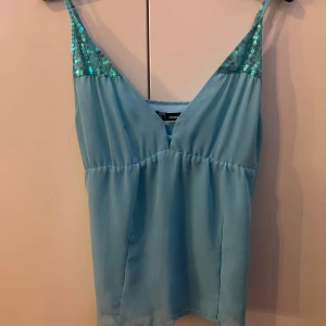 Blå linnetopp från ONLY - Snygg blå linnetopp från ONLY med paljettdetaljer på axelbanden. Perfekt för en glittrig touch till din outfit. Toppen har en enkel och stilren design med smala axelband.