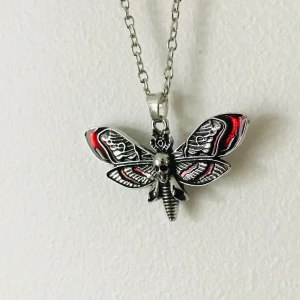 Halsband med fjärilshänge - Unikt halsband med ett detaljerat fjärilshänge i silverfärg med röda inslag. Kedjan är av metall och har en klassisk länkdesign. Perfekt för att ge en edgy touch till din stil.