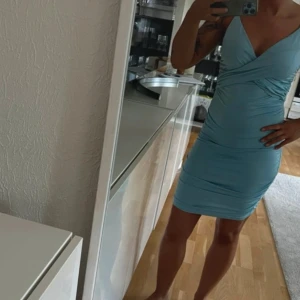 Ljusblå omlottklänning - Snygg ljusblå omlottklänning med smala axelband och draperad design. Perfekt för en somrig look. Klänningen har en tight passform som framhäver figuren. Aldrig använd 