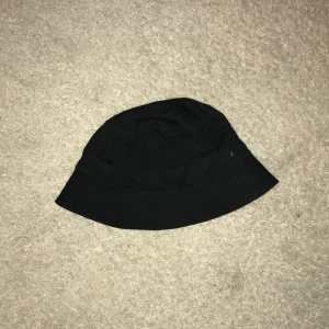 Svart bucket hat - Snygg och stilren svart bucket hat perfekt för alla tillfällen. Den har en klassisk form och är tillverkad i ett lätt material som gör den bekväm att bära. Passar både för soliga dagar och som en trendig accessoar.