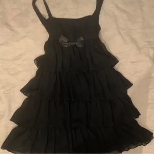 Super söt svart klänning med volanger!! - Jätte fin svart klänning med flera lager av volanger och en söt rosett framtill. Säljer för att den är för stor för mig :( super bra kvalitet!! (Laddar up igen för fri frakt)