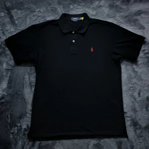 Ralph Lauren pike - Säljer en stilren svart pikétröja från Ralph Lauren med röd broderad logga på bröstet. Tröjan har korta ärmar och klassisk krage med knappar. Perfekt för en avslappnad men ändå snygg look. Storlek L, skick 10/10. Pris går att diskutera ✅