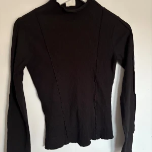 Svart ribbad polotröja - Snygg svart ribbad polotröja med lång ärm. Perfekt för kyligare dagar och kan enkelt matchas med olika outfits. Tröjan har en stilren design och är ett måste i garderoben.