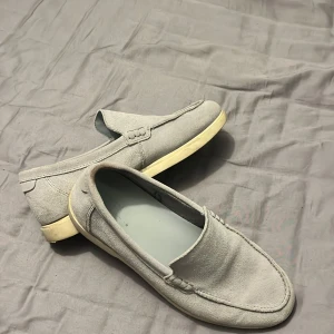 Grå loafers från Zara - Snygga grå loafers från Zara i mocka. Perfekta för en stilren look med en bekväm passform. De har en klassisk design med en ljus sula som ger en modern touch.