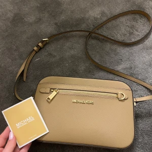 Beige axelväska från Michael Kors - Så snygg beige michael kors väska som är helt oanvänd! Säljer då den inte kommer till användning längre! Den har ett justerbart band och en kedja för design som kan sättas på och tas av. Flertal fickor och har inga defekter! Skriv privat för frågor eller fler bilder! 💕
